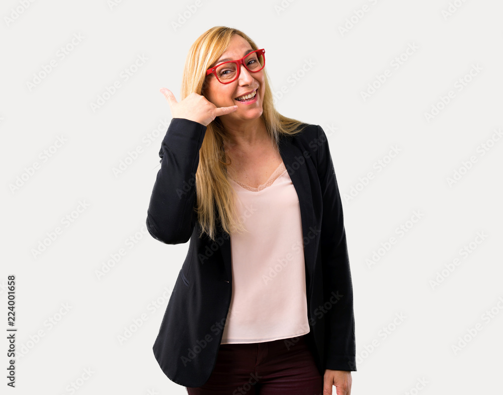 Middle-age blonde business woman with black jacket making phone gesture and speaking with someone. Call me back sign on isolated grey background Middle-age blonde business woman with black jacket making phone gesture and speaking with someone. Call me back sign on isolated grey background