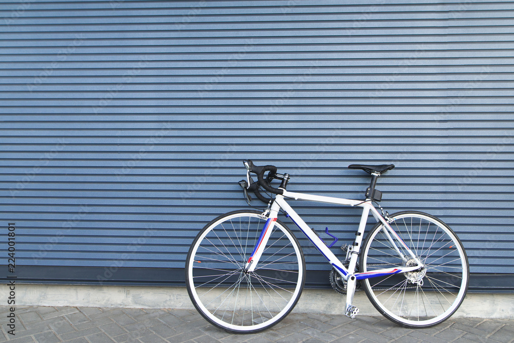 White highway bike stands on the background of a gray wall. Sports concept. Cycling Concept White highway bike stands on the background of a gray wall. Sports concept. Cycling Concept