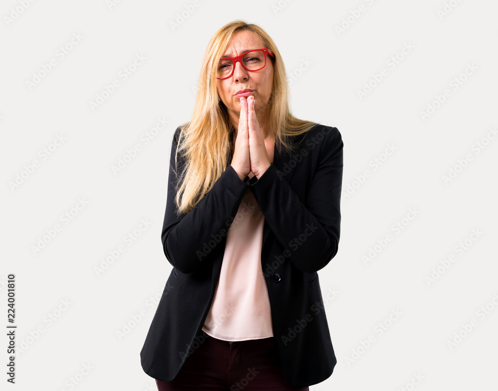 Middle-age blonde business woman with black jacket keeps palm together. Person asks for something on isolated grey background Middle-age blonde business woman with black jacket keeps palm together. Person asks for something on isolated grey background