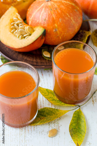 Two glasses with natural homemade juice and a fresh ripe pumpkin on an old wooden table. The concept of healthy eating. 