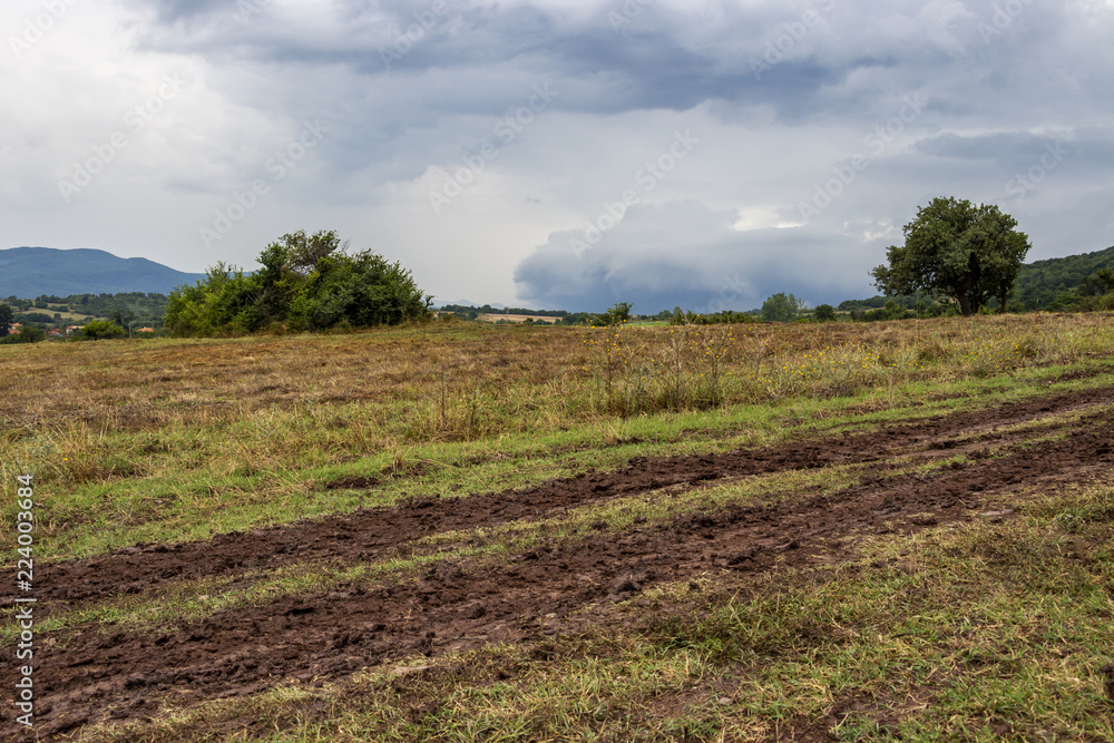 Muddy wheel tracks in a field at the foot of a Rhodope Mountains hill under dramatic stormy sky in Bulgaria Muddy wheel tracks in a field at the foot of a Rhodope Mountains hill under dramatic stormy sky in Bulgaria
