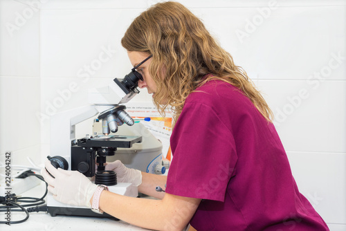 Young laboratory assistant looking through a microscope