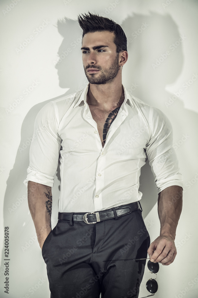 Elegant attractive young man with white shirt, leaning against wall, looking at camera Elegant attractive young man with white shirt, leaning against wall, looking at camera