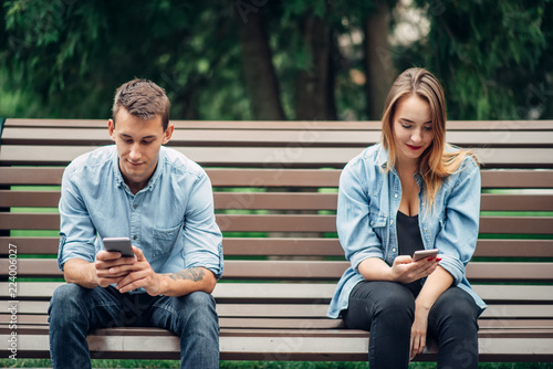 Phone addicted couple on the bench in park