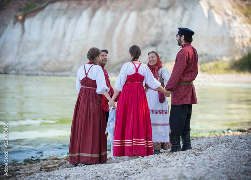 A group of people in Russian folk costumes dancing in a beautiful landscape, in the foreground is the accordion