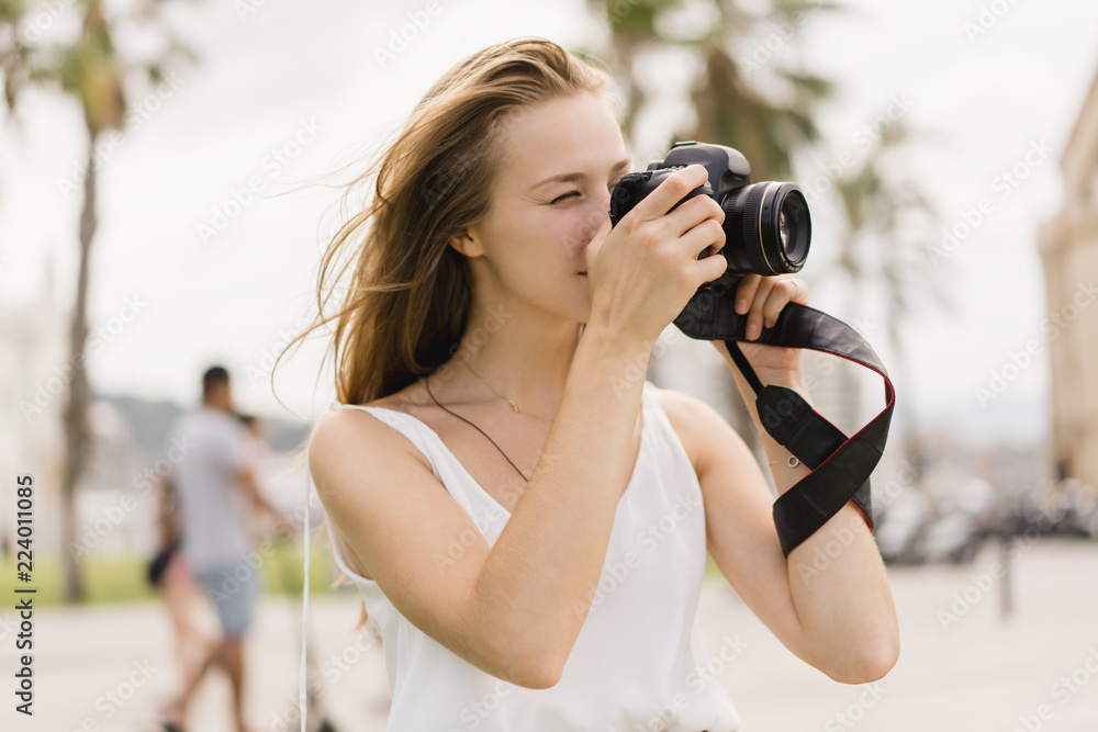 Professional female photographer taking pictures on a modern dslr camera in the park while walking around in the fresh air, young traveller girl using photo camera and shooting landscapes