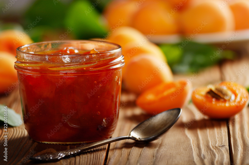 Glass Jar of Apricot jam on wooden table with ripe apricots at background Glass Jar of Apricot jam on wooden table with ripe apricots at background