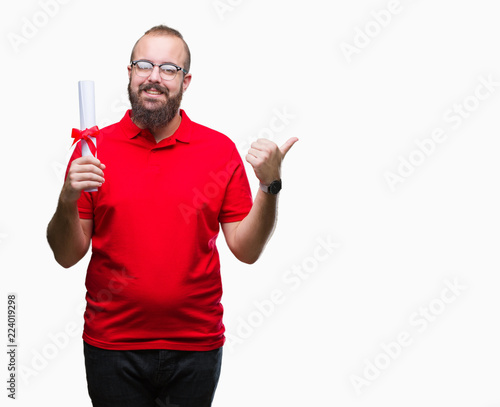 Young hipster man wearing glasses and holding degree over isolated background pointing and showing with thumb up to the side with happy face smiling