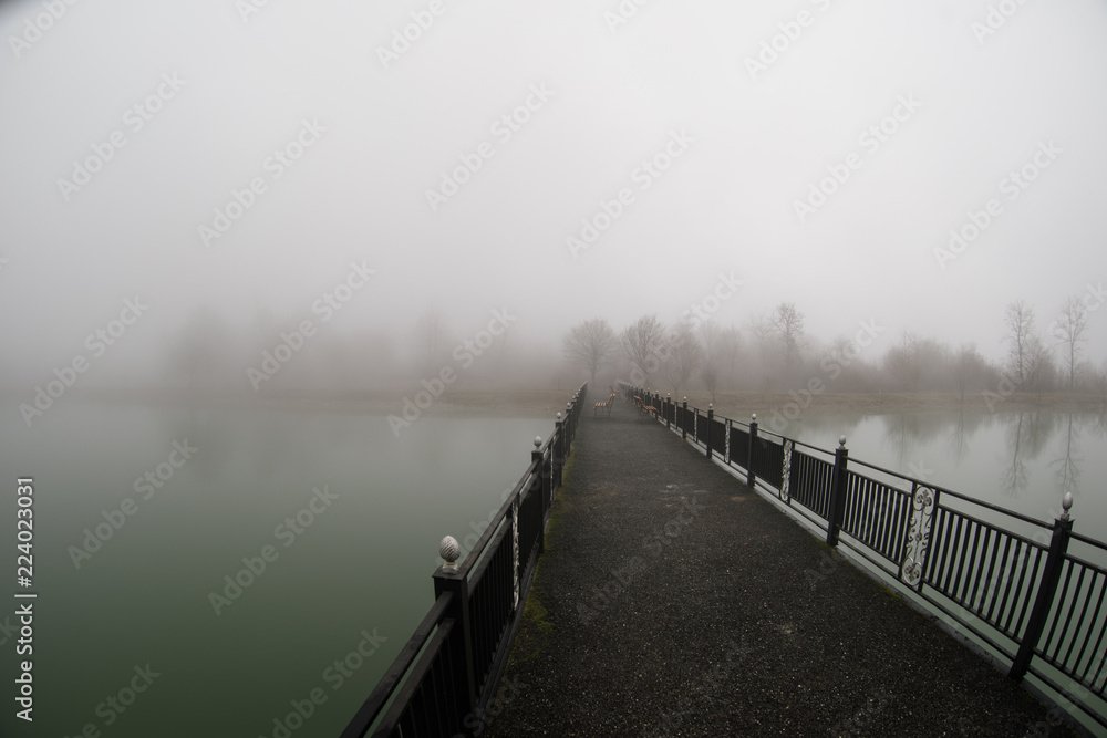 Amazing landscape of bridge reflect on surface water of lake, fog evaporate from pond make romantic scene or Beautiful bridge on lake with trees at fog.