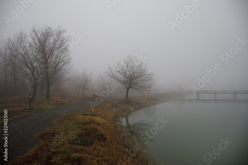 Amazing landscape of bridge reflect on surface water of lake, fog evaporate from pond make romantic scene or Beautiful bridge on lake with trees at fog.