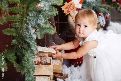 happy little girl in white dress puts firewood in the Christmas wooden brown decorated room interior