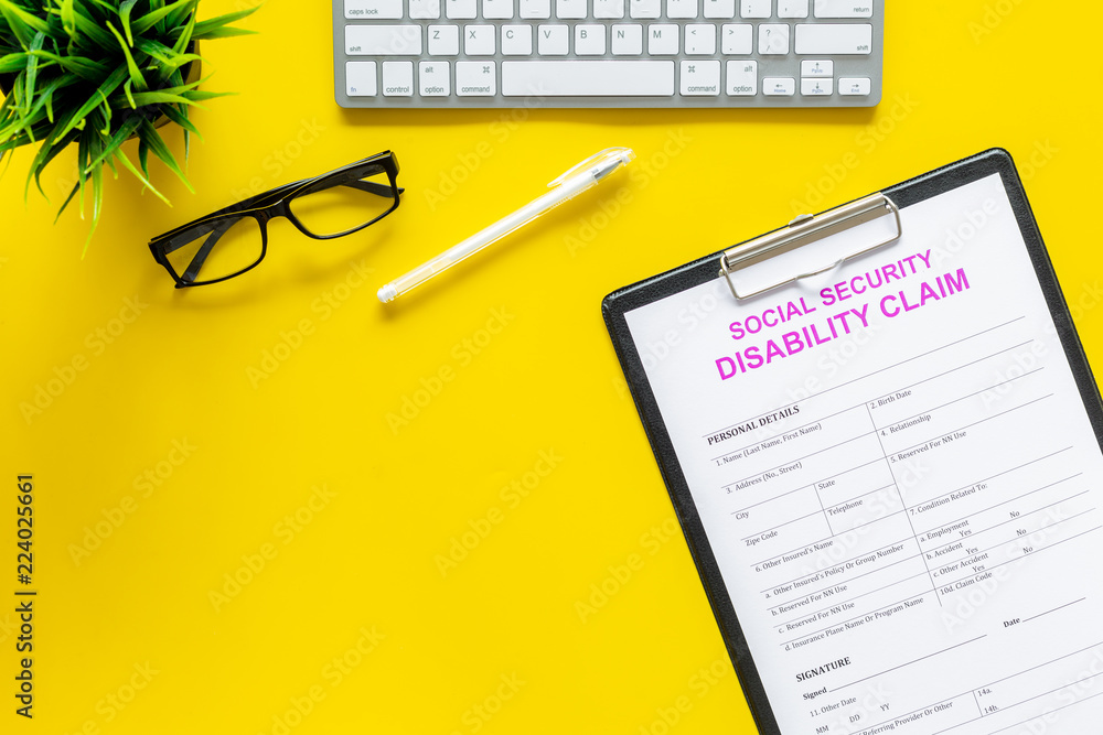 Social security. Disability claim form near glasses on office desk on yellow background top view copy space Social security. Disability claim form near glasses on office desk on yellow background top view copy space