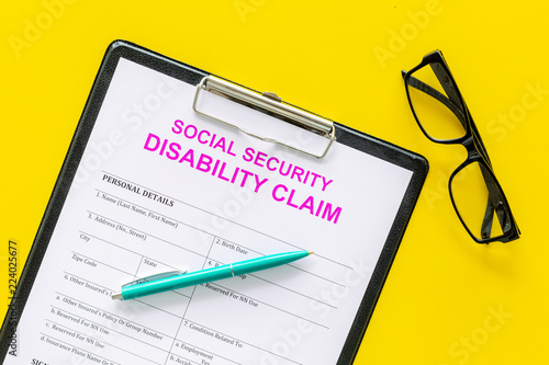 Social security. Disability claim form near pen and glasses on yellow background top view photo