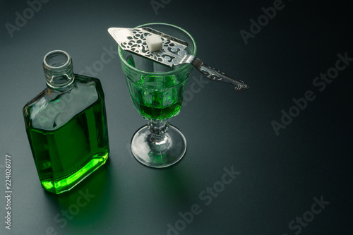 an absinthe bottle, a glass of absinthe and a stainless steel slotted spoon with the sugar cube on the table
