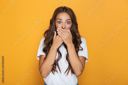 Image of surprised woman 20s with long hair covering mouth with hands, isolated over yellow background