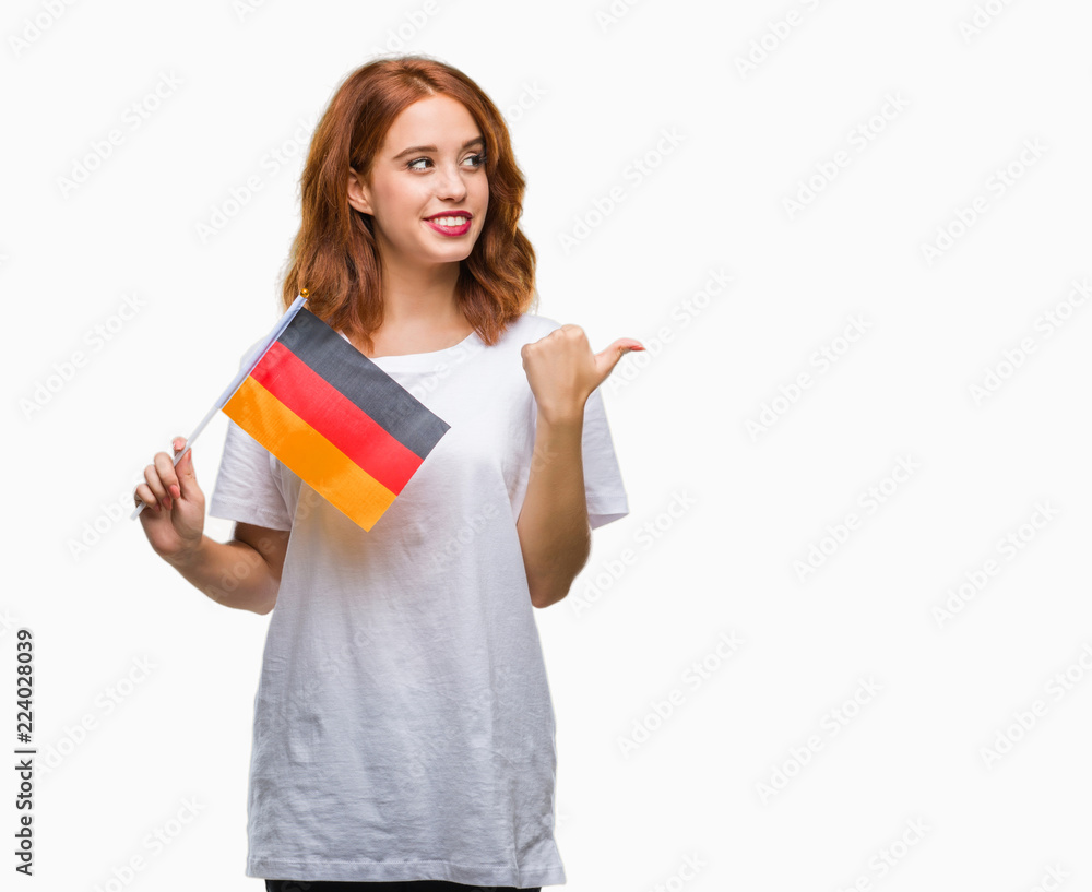 Young beautiful woman holding flag of germany over isolated background pointing and showing with thumb up to the side with happy face smiling Young beautiful woman holding flag of germany over isolated background pointing and showing with thumb up to the side with happy face smiling