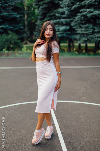 Charming brunette female dressed in a pink dress posing on the basketball court.