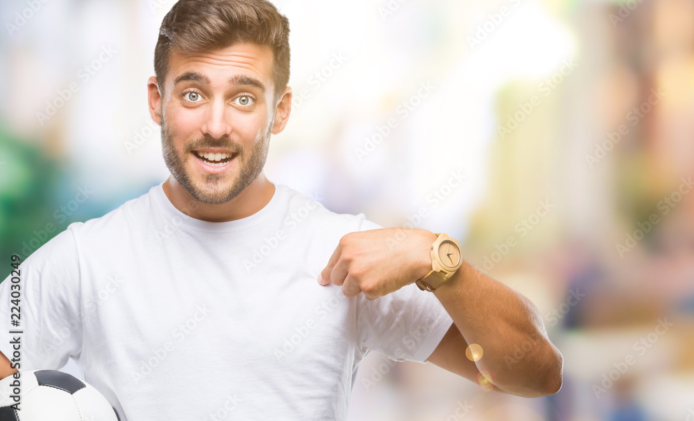 Young handsome man holding soccer football ball over isolated background with surprise face pointing finger to himself Young handsome man holding soccer football ball over isolated background with surprise face pointing finger to himself
