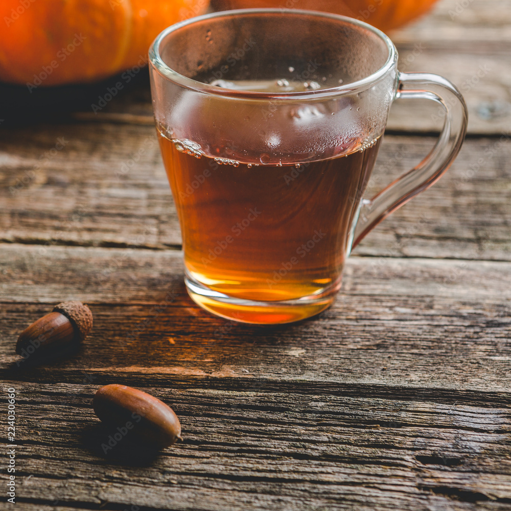 Autumn background on wooden table with a pumpkins, a glass cup of tea and acorns Autumn background on wooden table with a pumpkins, a glass cup of tea and acorns