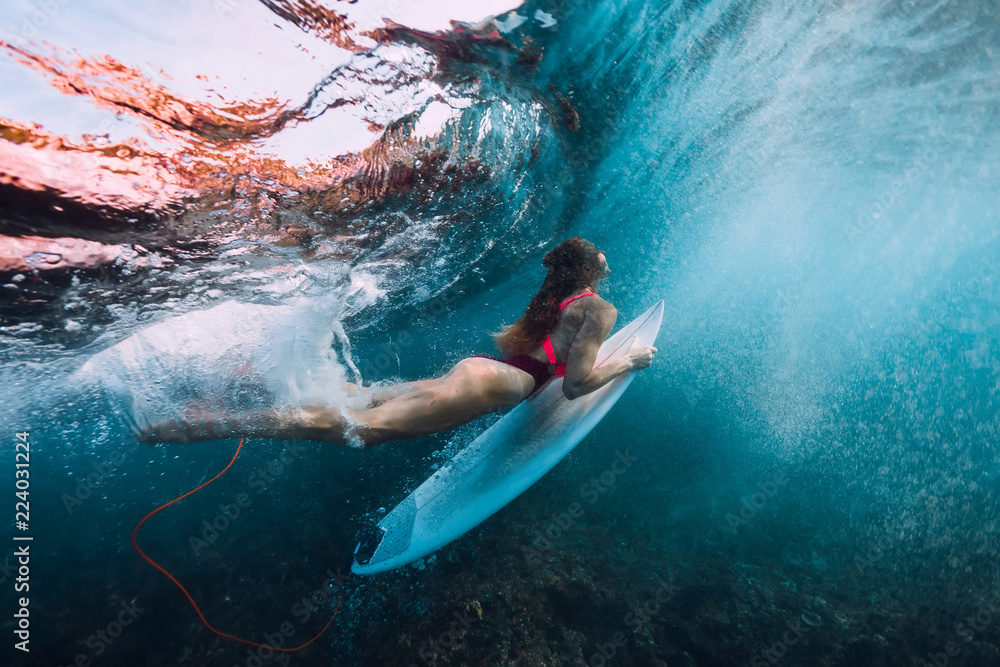 Surfer girl with surfboard dive underwater with under big wave.