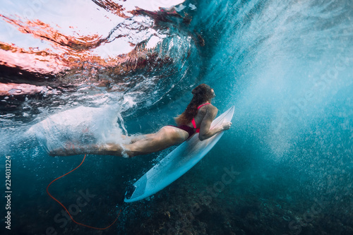 Surfer girl with surfboard dive underwater with under big wave.