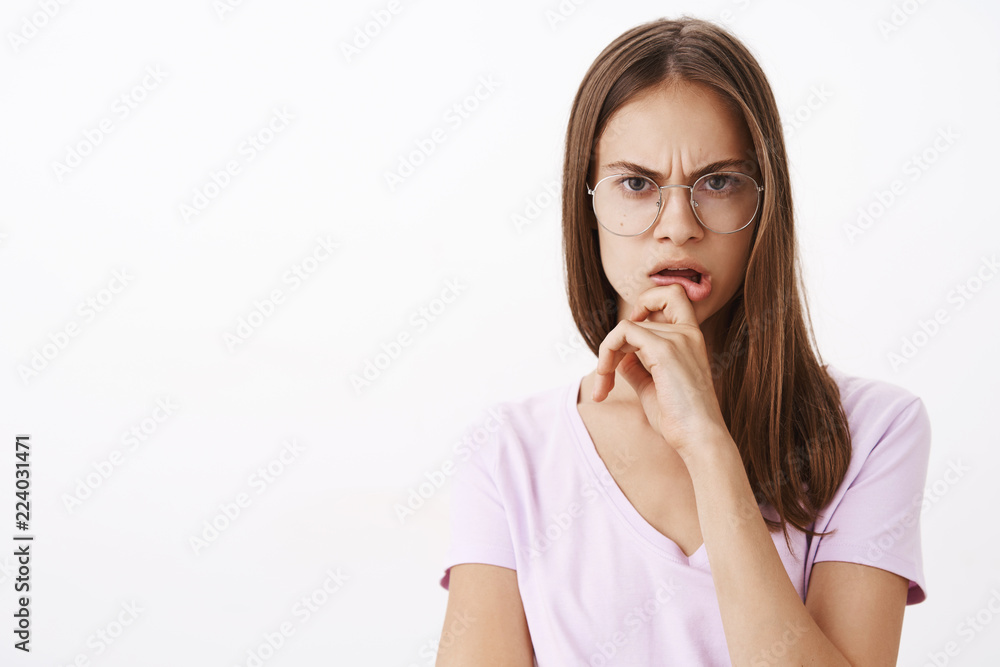 Woman hearing out strange suspicious story being perplexed and doubtful frowning touching lip and staring with disbelief and concerned look at camera standing in glasses and blouse over white wall Woman hearing out strange suspicious story being perplexed and doubtful frowning touching lip and staring with disbelief and concerned look at camera standing in glasses and blouse over white wall