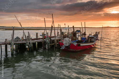 Sunset landscape of artisanal fishing boats in the old wooden pier. Carrasqueira is a tourist destination for visitors to the coast of Alentejo near Lisbon. © aroxopt