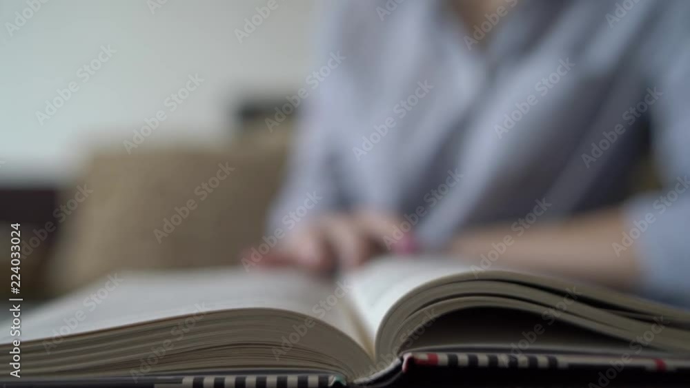 Girl flips a page while reading a book, blurry background