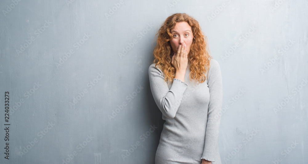 Young redhead woman over grey grunge wall cover mouth with hand shocked with shame for mistake, expression of fear, scared in silence, secret concept Young redhead woman over grey grunge wall cover mouth with hand shocked with shame for mistake, expression of fear, scared in silence, secret concept