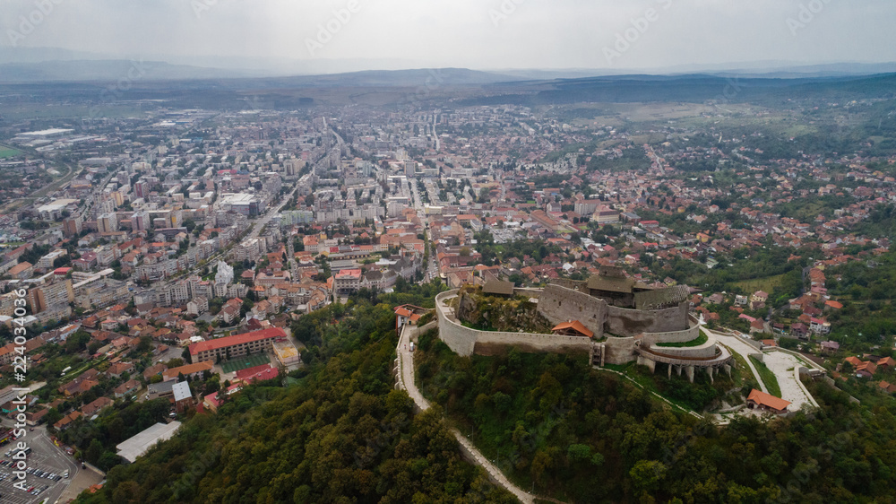 Aerial view of Deva Castle with the town in the background on a cloudy sky.