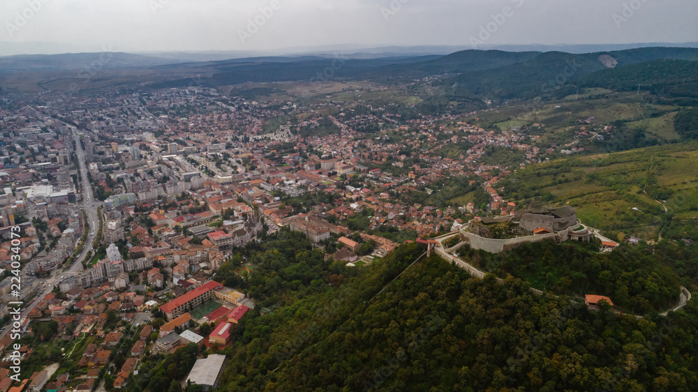 Aerial view of Deva Castle with the town in the background on a cloudy sky.