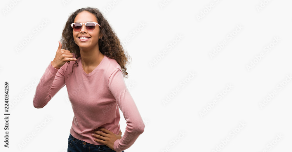 Beautiful young hispanic woman wearing sunglasses smiling doing phone gesture with hand and fingers like talking on the telephone. Communicating concepts.
