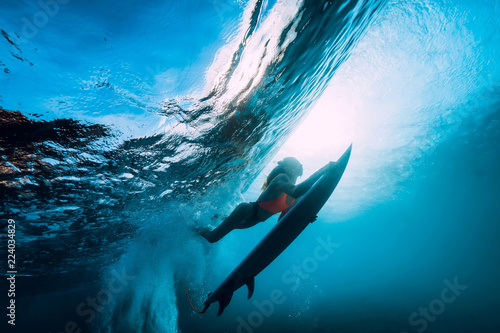 Surfer girl with surfboard dive underwater with fun under big ocean wave. © artifirsov