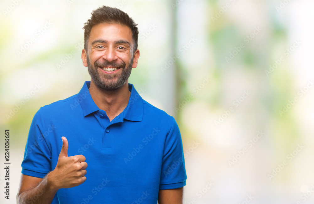 Adult hispanic man over isolated background doing happy thumbs up gesture with hand. Approving expression looking at the camera with showing success. Adult hispanic man over isolated background doing happy thumbs up gesture with hand. Approving expression looking at the camera with showing success.