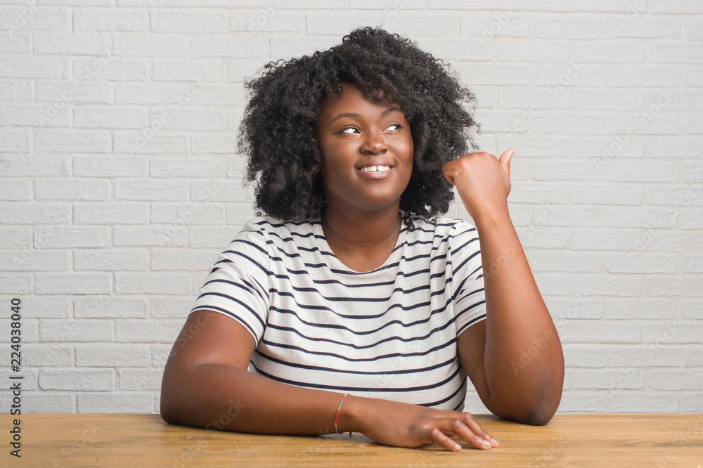 Young african american woman sitting on the table at home smiling with ...