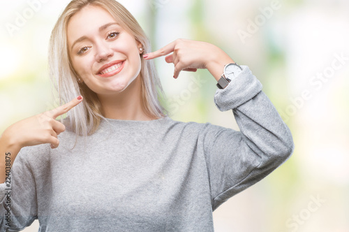 Young blonde woman over isolated background smiling confident showing and pointing with fingers teeth and mouth. Health concept.