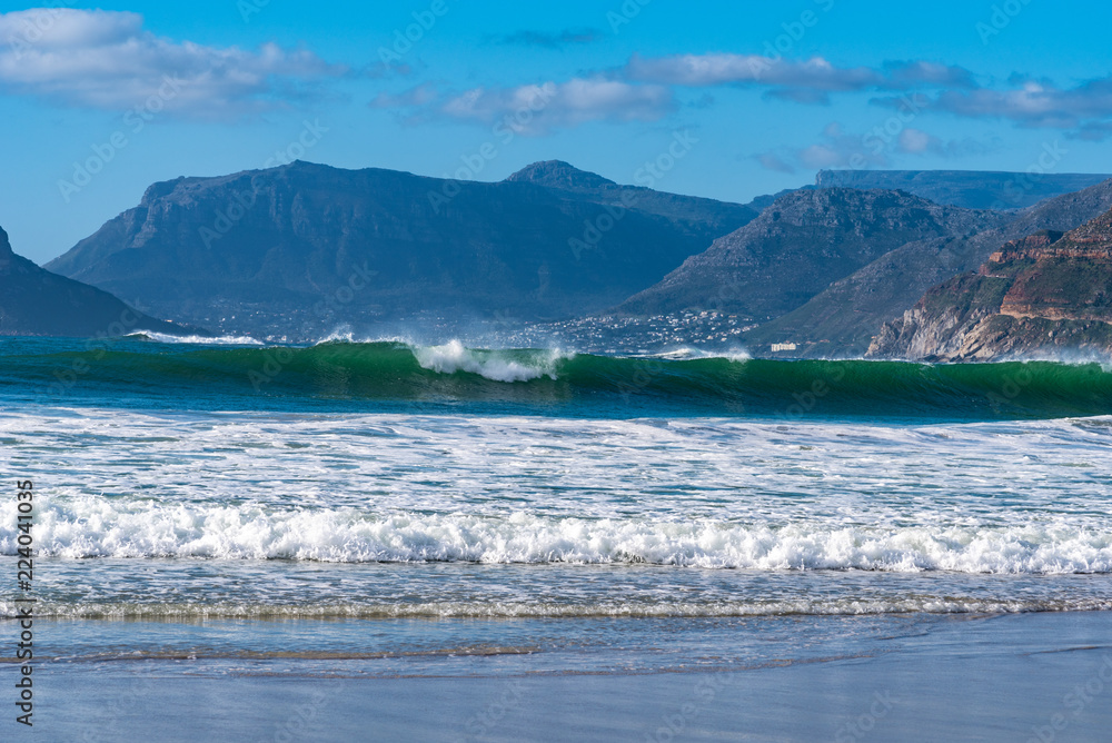 Obraz premium Beach and waves across a bay with beautiful mountains in distance.
