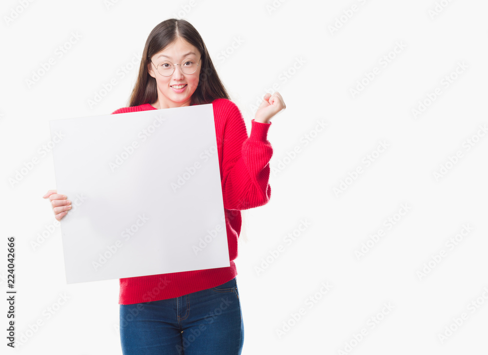 Young Chinese woman over isolated background holding blank banner screaming proud and celebrating victory and success very excited, cheering emotion Young Chinese woman over isolated background holding blank banner screaming proud and celebrating victory and success very excited, cheering emotion