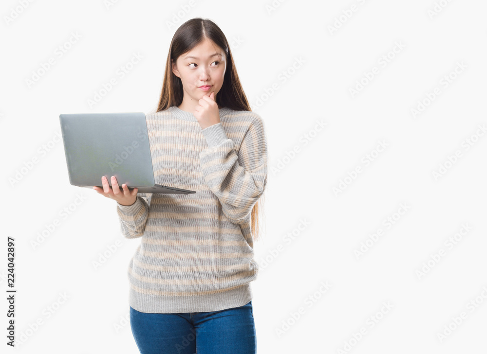 Young Chinese woman over isolated background using computer laptop serious face thinking about question, very confused idea Young Chinese woman over isolated background using computer laptop serious face thinking about question, very confused idea