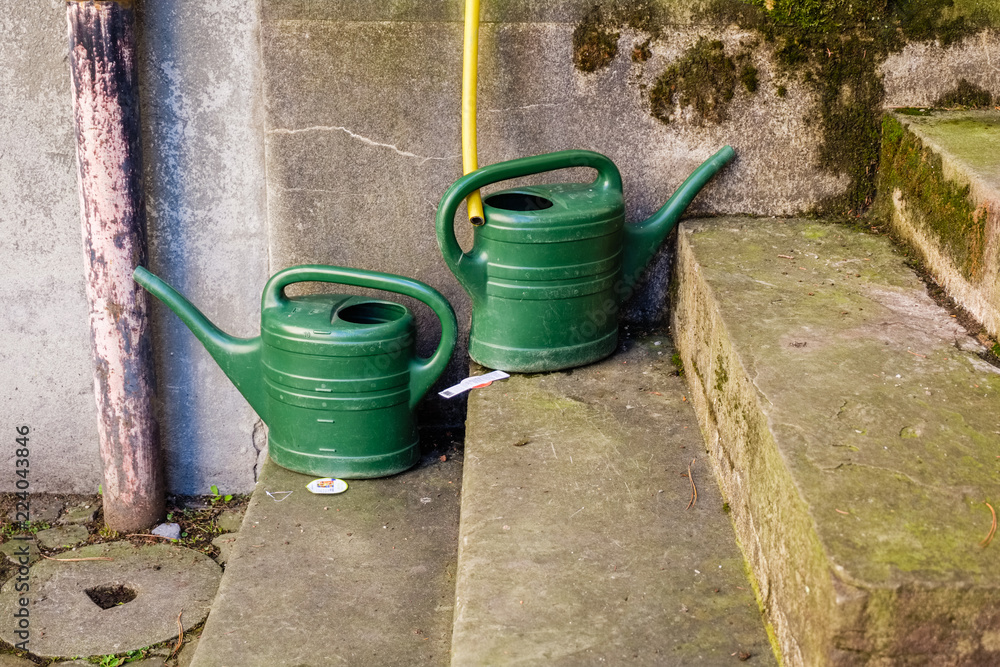Two empty green watering cans are waiting on a stone staircase to be used Two empty green watering cans are waiting on a stone staircase to be used