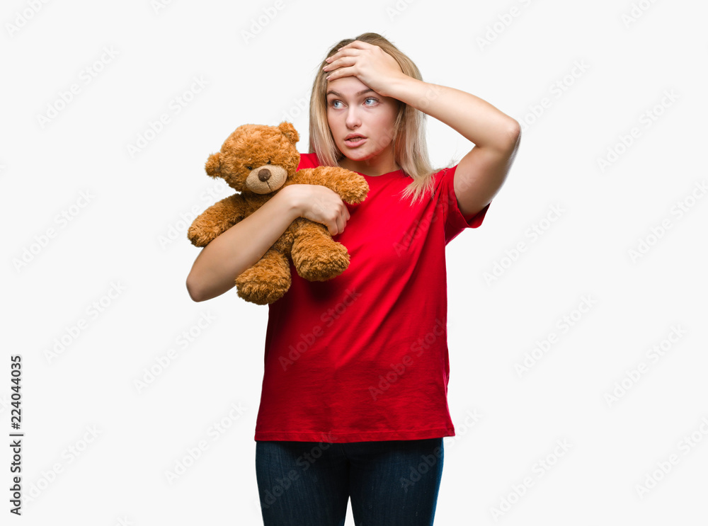 Young caucasian woman holding cute teddy bear over isolated background stressed with hand on head, shocked with shame and surprise face, angry and frustrated. Fear and upset for mistake. Young caucasian woman holding cute teddy bear over isolated background stressed with hand on head, shocked with shame and surprise face, angry and frustrated. Fear and upset for mistake.