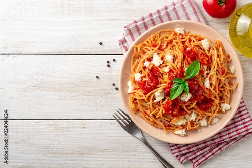 Spaghetti pasta with tomato sauce, mozzarella cheese and fresh basil in plate on white wooden background. Top view. Copy space.
