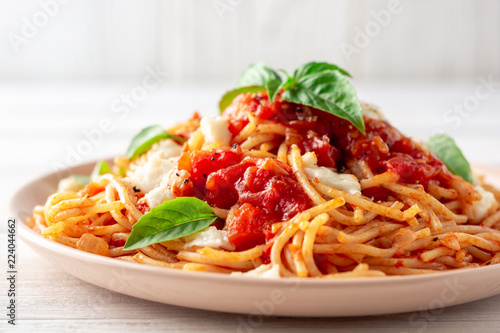 Spaghetti pasta with tomato sauce, mozzarella cheese and fresh basil in plate on white wooden background. Selective focus.