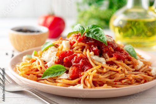 Spaghetti pasta with tomato sauce, mozzarella cheese and fresh basil in plate on white wooden background. Selective focus.