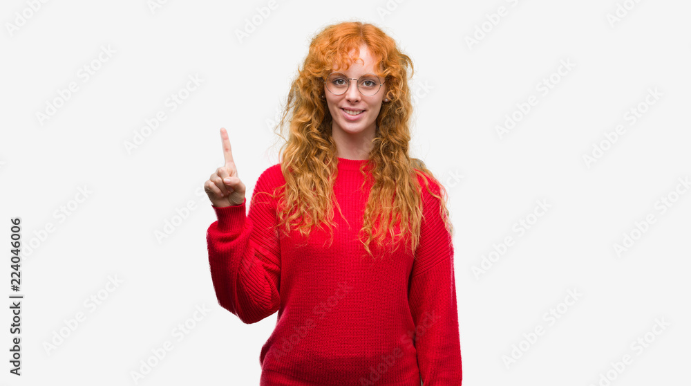 Young redhead woman wearing red sweater showing and pointing up with finger number one while smiling confident and happy. Young redhead woman wearing red sweater showing and pointing up with finger number one while smiling confident and happy.