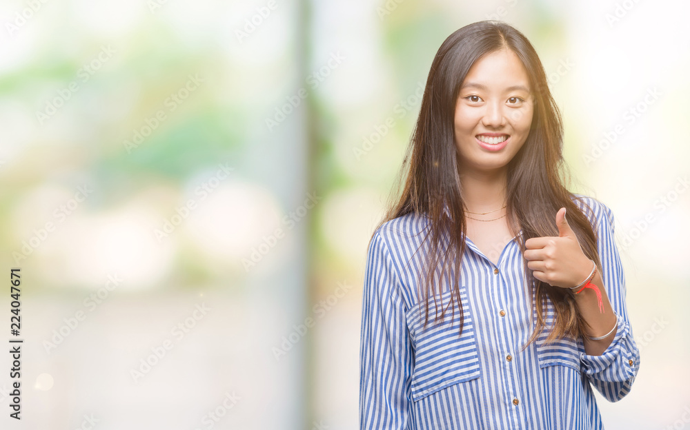Young asian woman over isolated background doing happy thumbs up gesture with hand. Approving expression looking at the camera with showing success. Young asian woman over isolated background doing happy thumbs up gesture with hand. Approving expression looking at the camera with showing success.