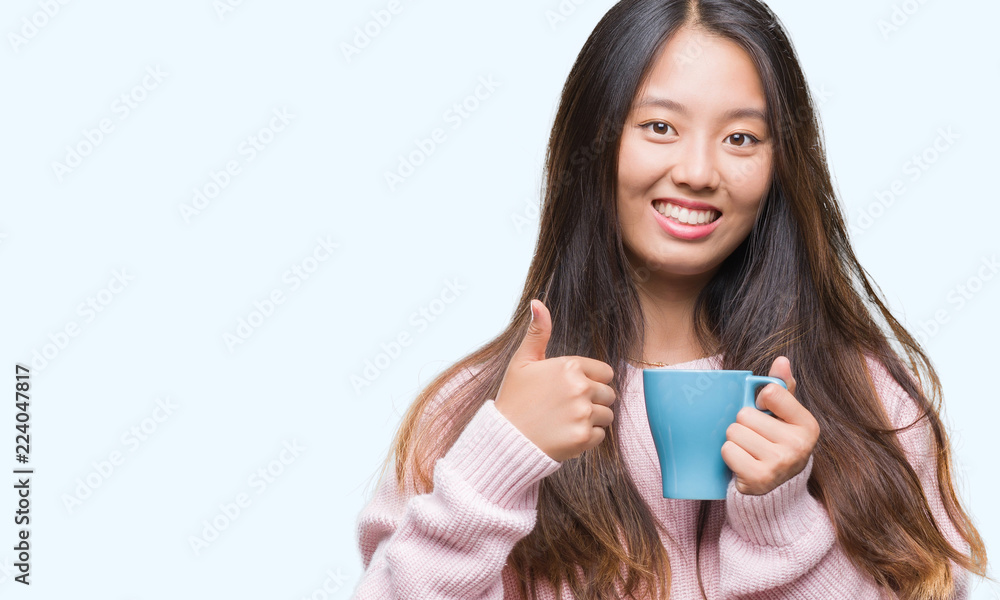 Young asian woman drinking coffee over isolated background happy with big smile doing ok sign, thumb up with fingers, excellent sign Young asian woman drinking coffee over isolated background happy with big smile doing ok sign, thumb up with fingers, excellent sign