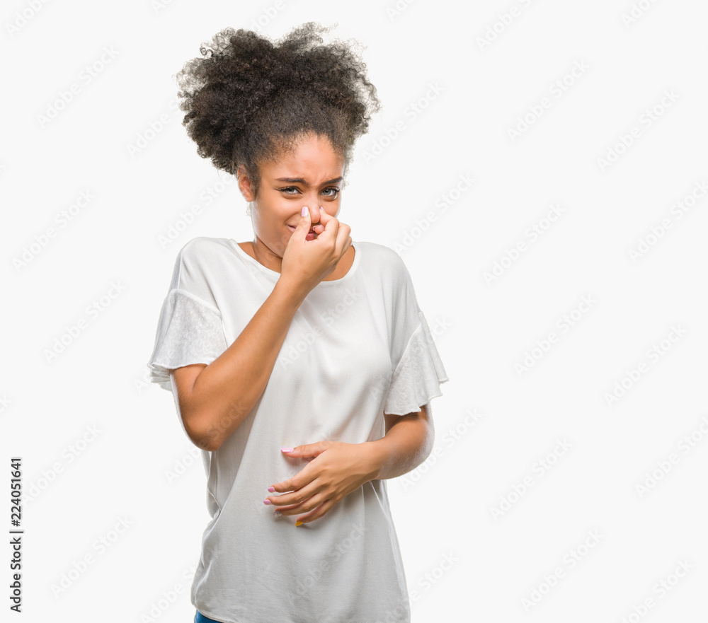 Young afro american woman over isolated background smelling something stinky and disgusting, intolerable smell, holding breath with fingers on nose. Bad smells concept. Young afro american woman over isolated background smelling something stinky and disgusting, intolerable smell, holding breath with fingers on nose. Bad smells concept.