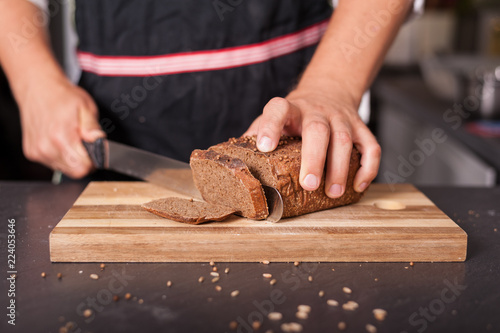 A man is cutting a whole-meal loaf of bread on wooden board.