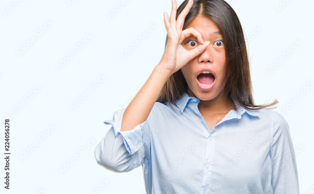 Young asian business woman over isolated background doing ok gesture shocked with surprised face, eye looking through fingers. Unbelieving expression.